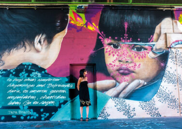 Eine Frau steht vor einer Wand mit grellen Grafittis