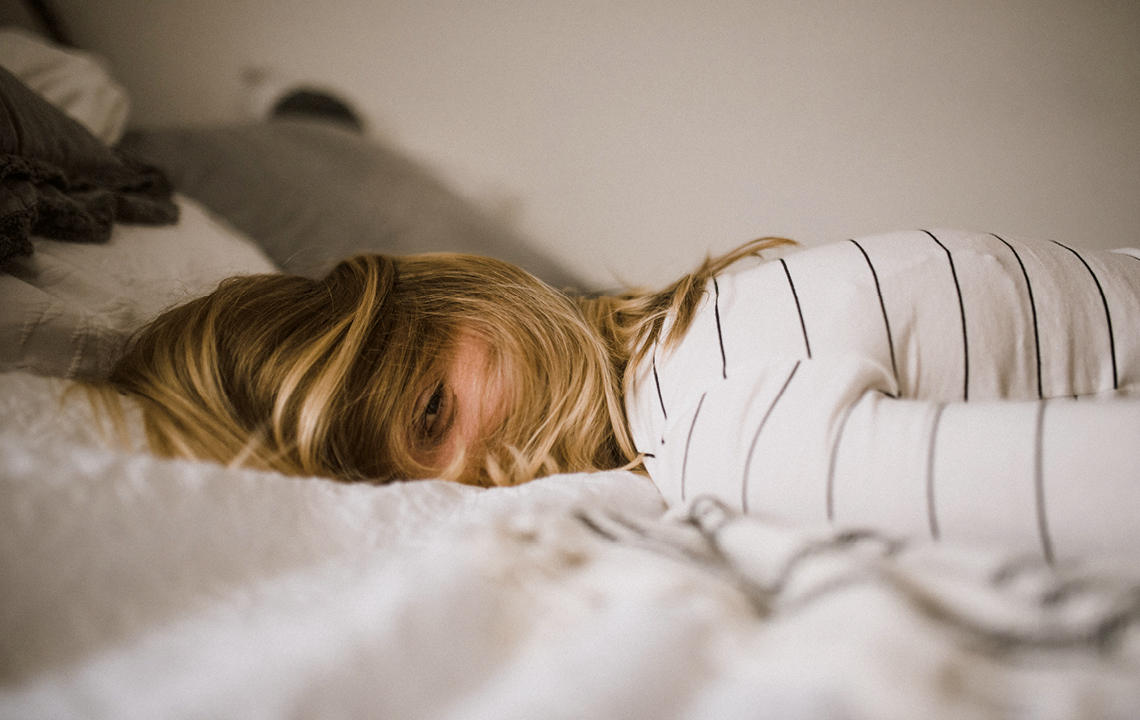 Eine Frau liegt auf dem Bett. Ihre Haare bedecken ihr Gesicht fast vollständig. Lediglich ihr Auge lässt ein Lächeln erahnen.