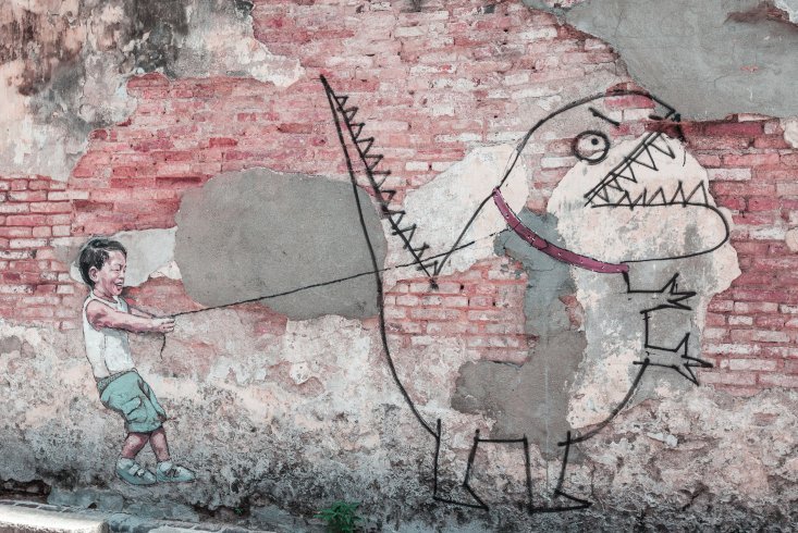 Zeichnung eines kleinen Jungen, der einen Comic-Dinosaurier an einer Leite hält als Streetart an einer Mauer. Link führt zur Leseprobe "Achtsamkeit mit Kindern leben"