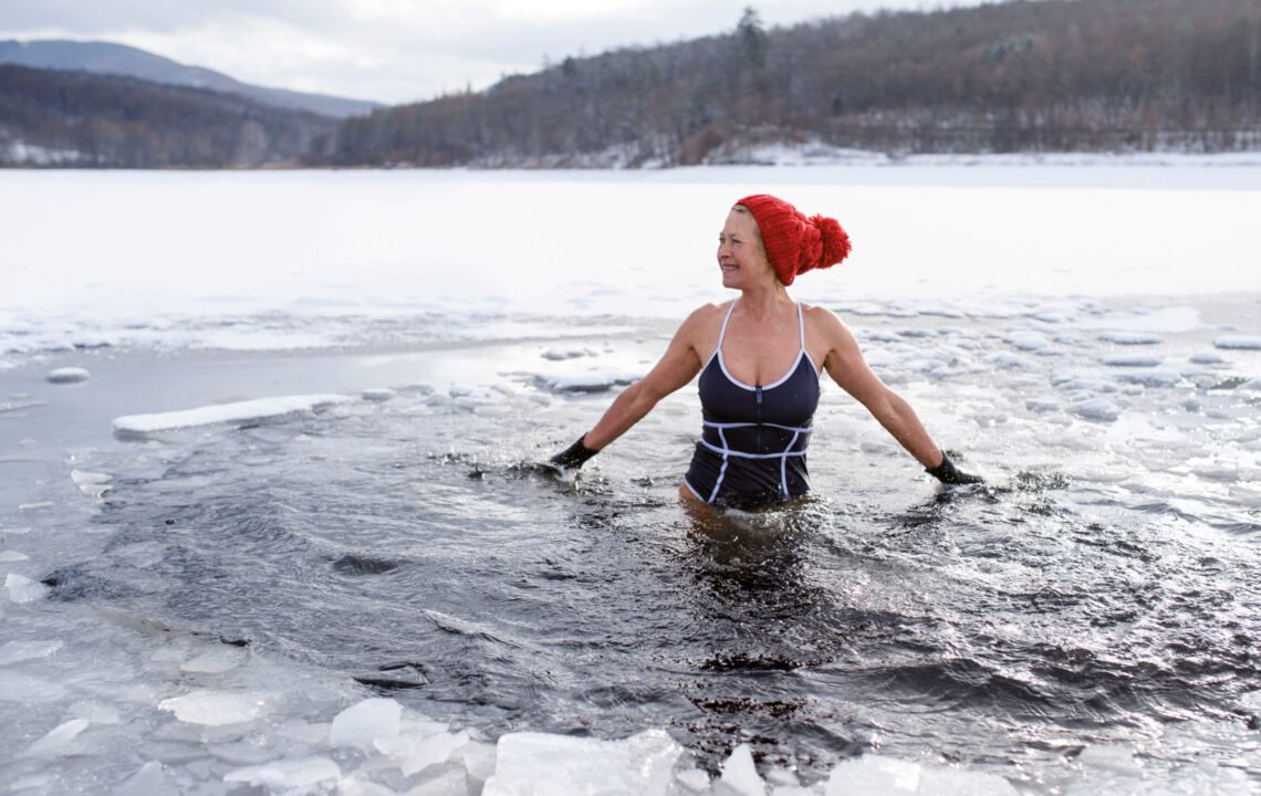 Eine Frau lacht, während sie in einem Loch in der Eisdecke eines zugefrorenen Sees badet