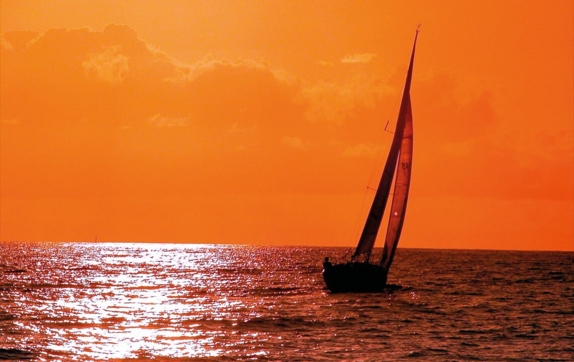 Ein kleines Segelboot auf dem Wasser vor rotem Abendhimmel