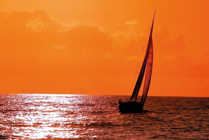 Ein kleines Segelboot auf dem Wasser vor rotem Abendhimmel. Link führt zu Leseprobe des Beitrags "Das Potenzial der Krise" von Anke Precht