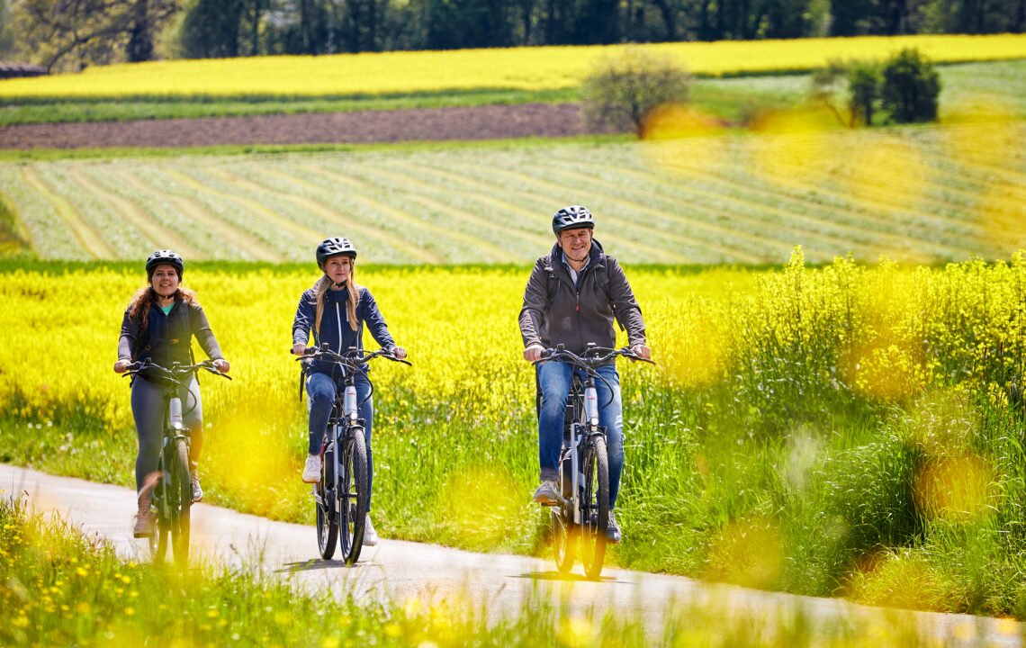 Eine dreiköpfige Familie fährt mit dem Fahrrad durch eine frühlingshafte Landschaft